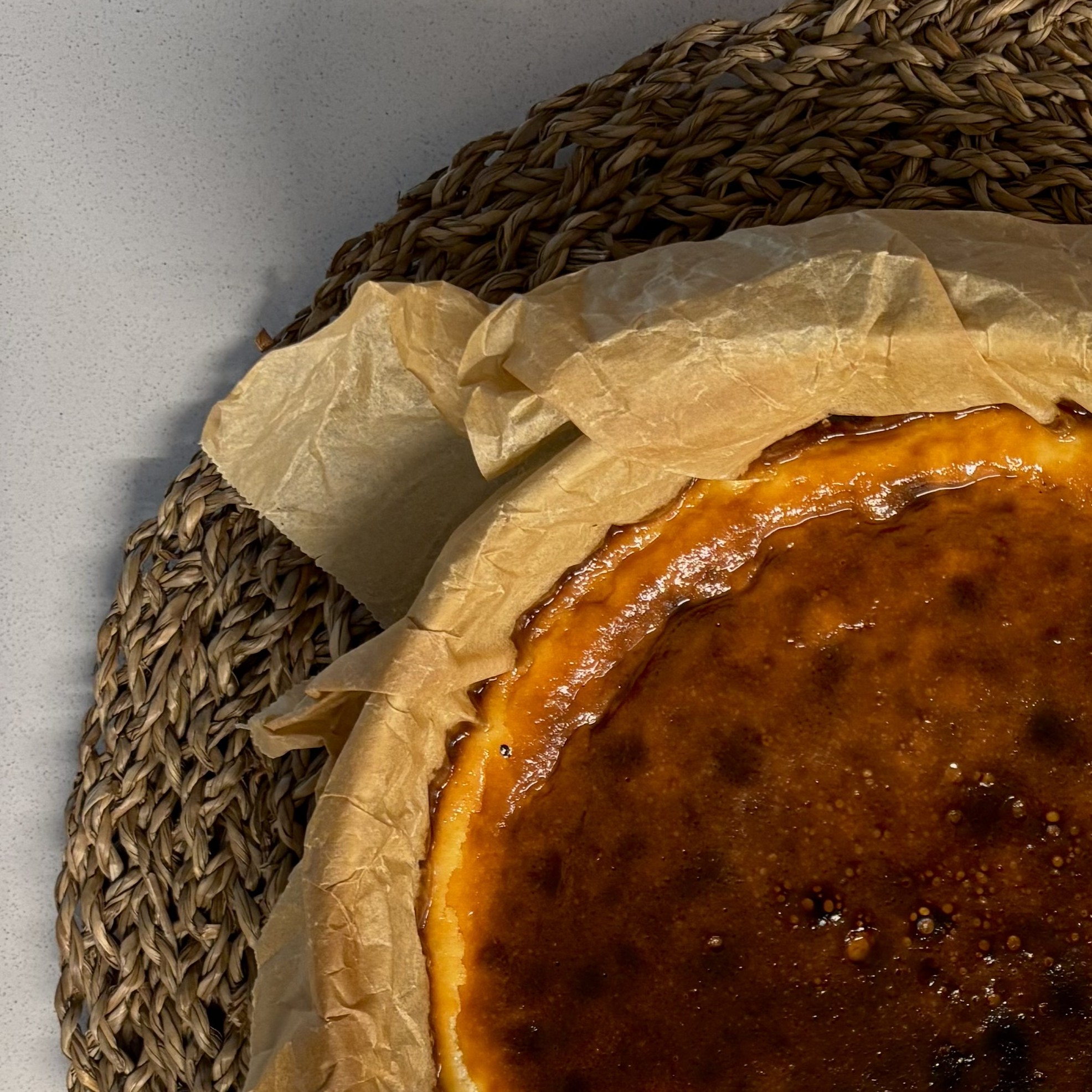 A whole BASCA Basque cheesecake with a dark burnt top, fresh out of the oven on parchment paper